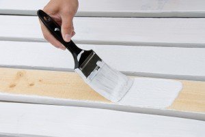 A painter primes the wooden slats of a fence that is being constructed.